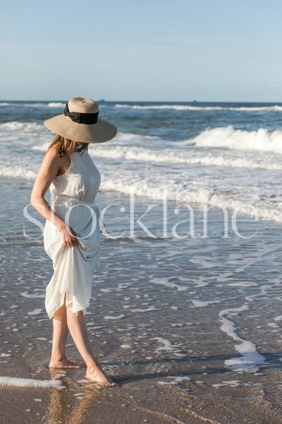 Vertical stock photo of a woman wearing a white dress walking into the water.