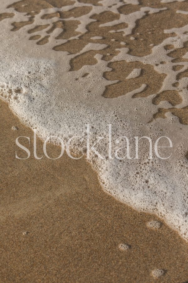 Vertical stock photo of the edge of the water on the beach.