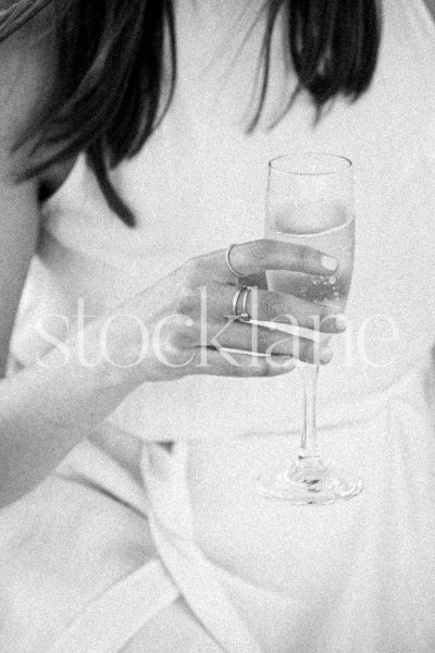 Vertical black and white photo of a woman wearing a white dress holding a glass of champagne.