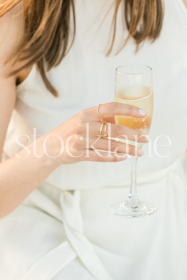 Vertical stock photo of a woman wearing a white dress holding a glass of champagne.