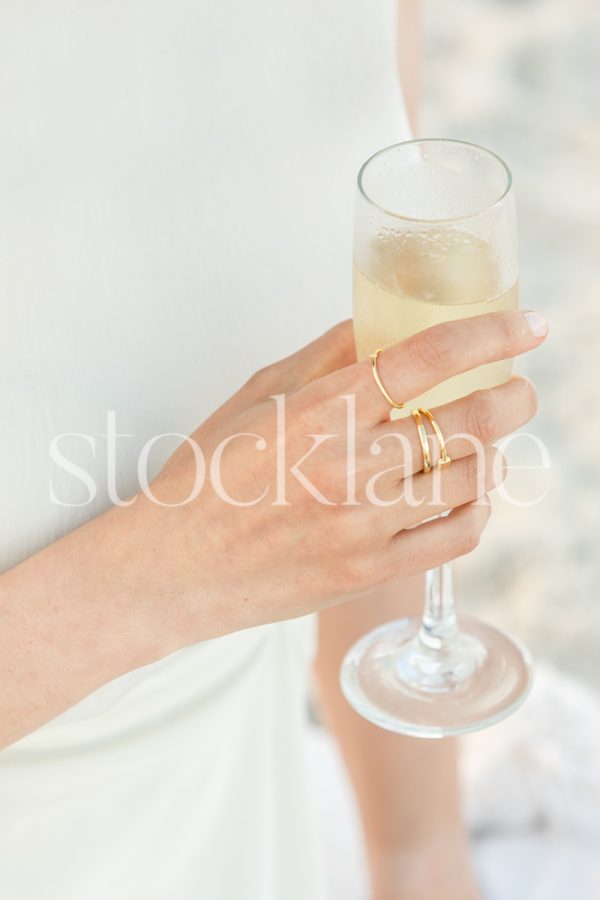 Vertical stock photo of a woman wearing a white dress holding a glass of champagne.