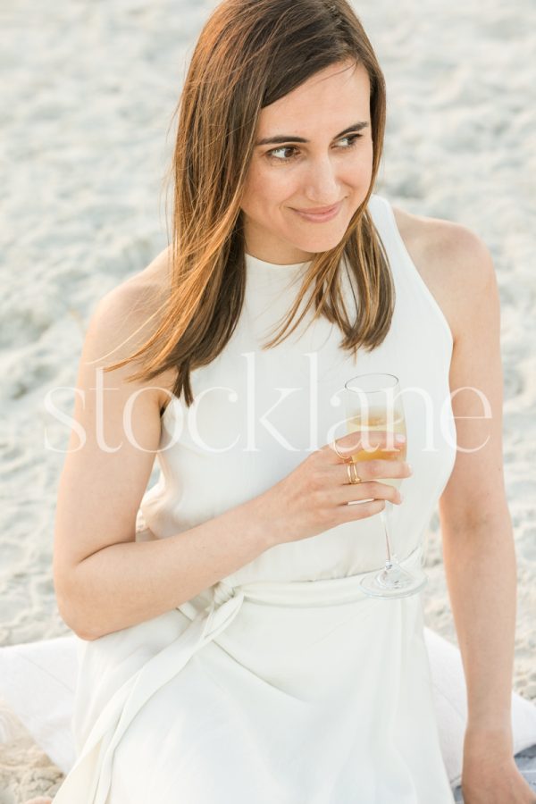 Vertical stock photo of a woman wearing a white dress holding a glass of champagne.