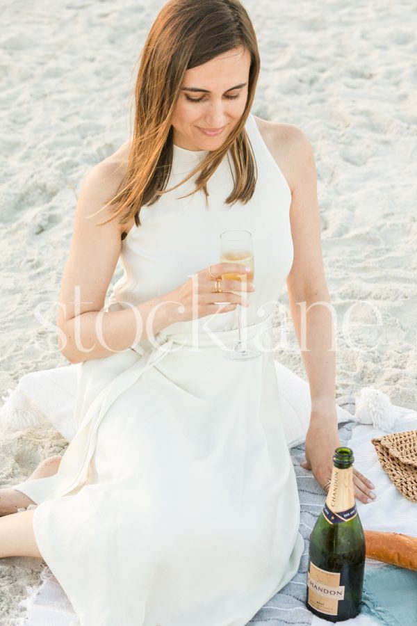 Vertical stock photo of a woman wearing a white dress holding a glass of champagne.