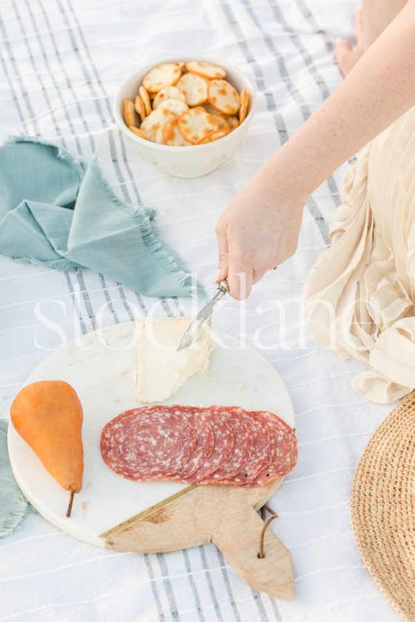 Vertical stock photo of a woman cutting a piece of cheese at a picnic.