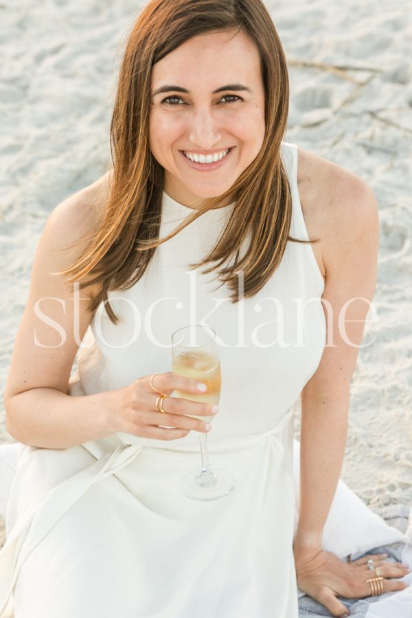 Vertical stock photo of a woman wearing a white dress holding a glass of champagne.