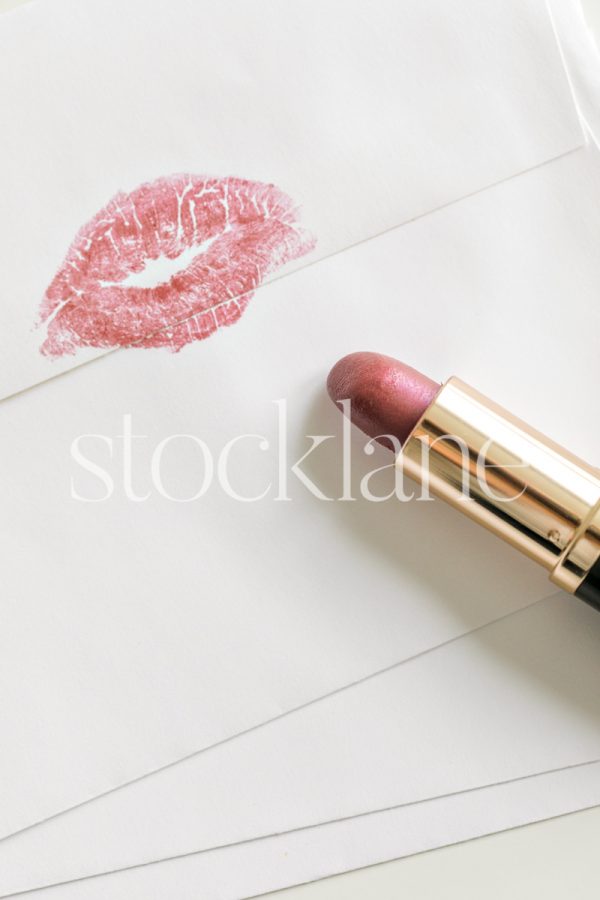 Vertical stock photo of an envelope with a kiss lipstick mark and a pink lipstick.