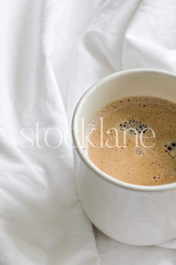 Vertical stock photo of a cup of coffee on a white bed.