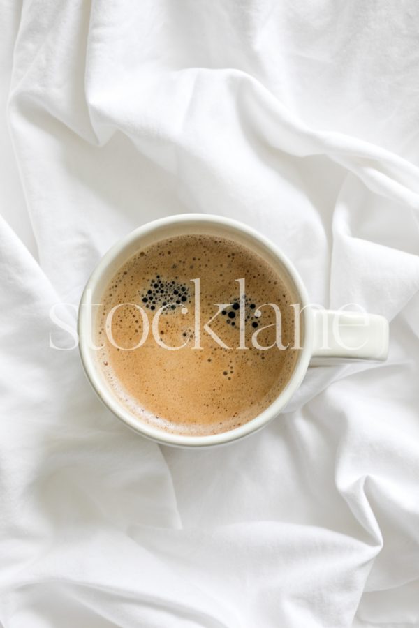 Vertical stock photo of a cup of coffee on a white bed.