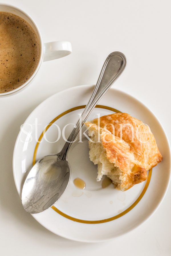 Vertical stock photo of a plate with a spoon, a half-eaten croissant, and a cup of coffee.