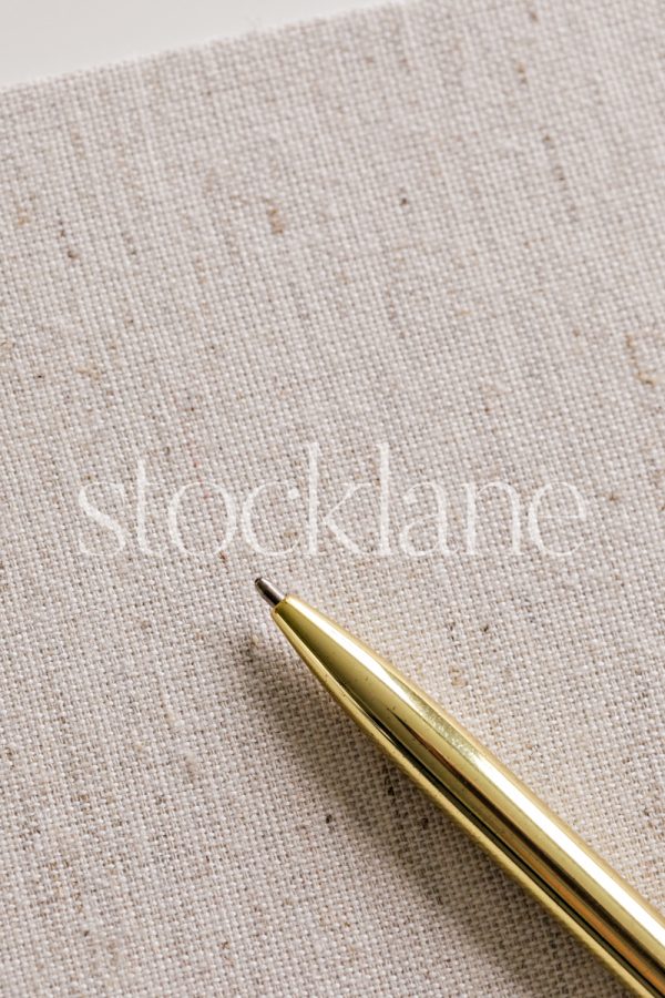 Vertical stock photo of a gold pen on a linen book.