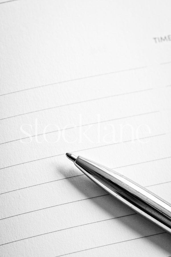 Vertical black and white photo of a pen on a notebook.