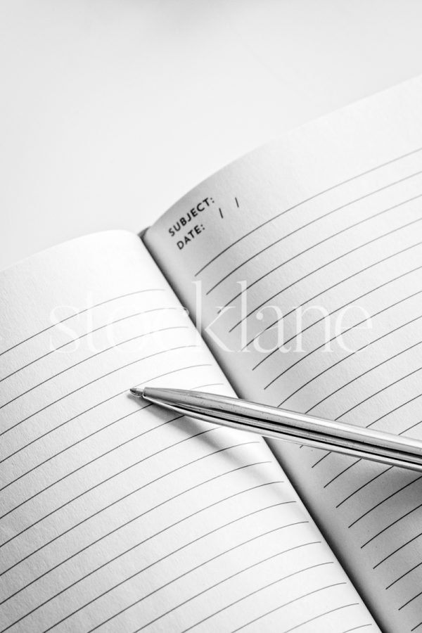 Vertical black and white stock photo of a pen on a notebook.