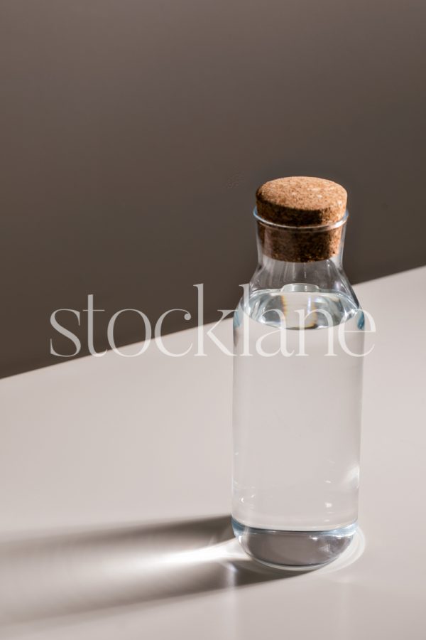 Vertical stock photo of a backlit water bottle with a cork top.