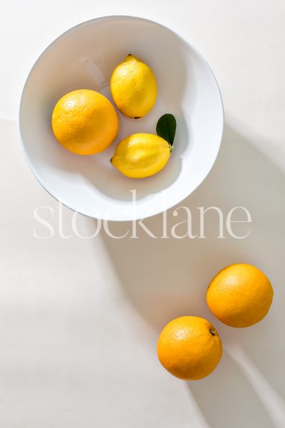 Vertical stock photo of a white bowl with oranges and lemons.