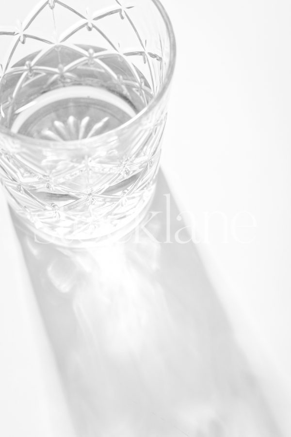 Vertical black and white stock photo of a glass with water, with light reflecting through it, on a white background.