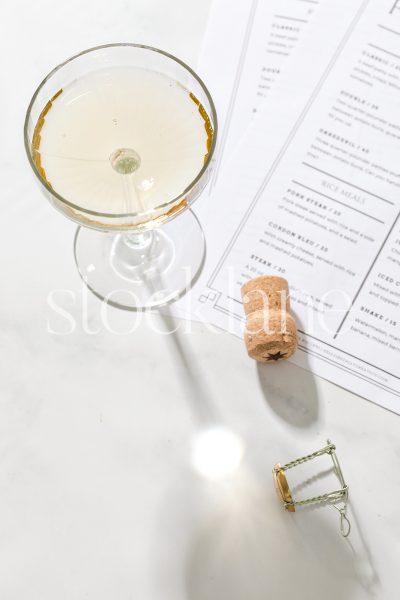 Vertical stock photo of a coupe glass of champagne next to a cork and restaurant menus.