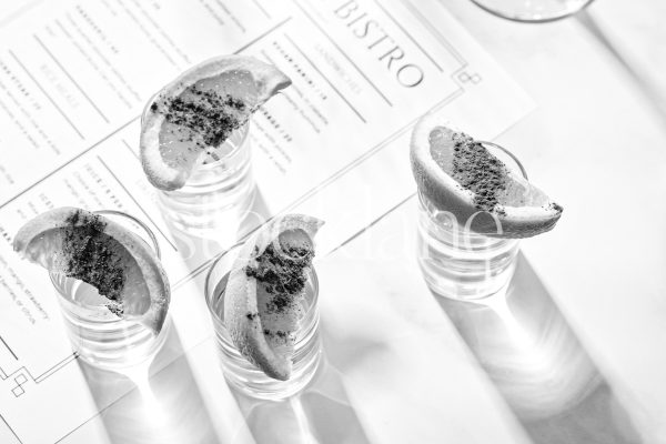 Horizontal black and white stock photo of shot glasses with sliced oranges on them on a restaurant menu.