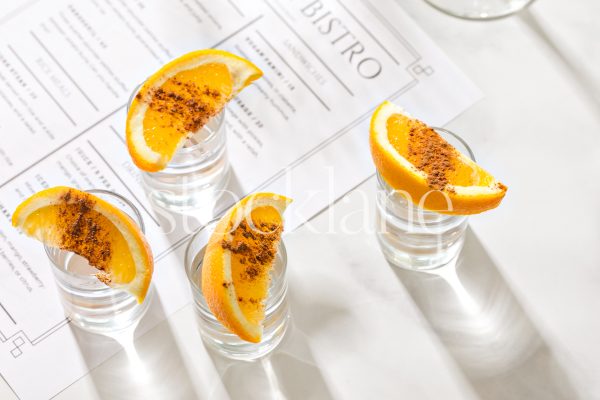 Horizontal stock photo of shot glasses with sliced oranges on them on a restaurant menu.