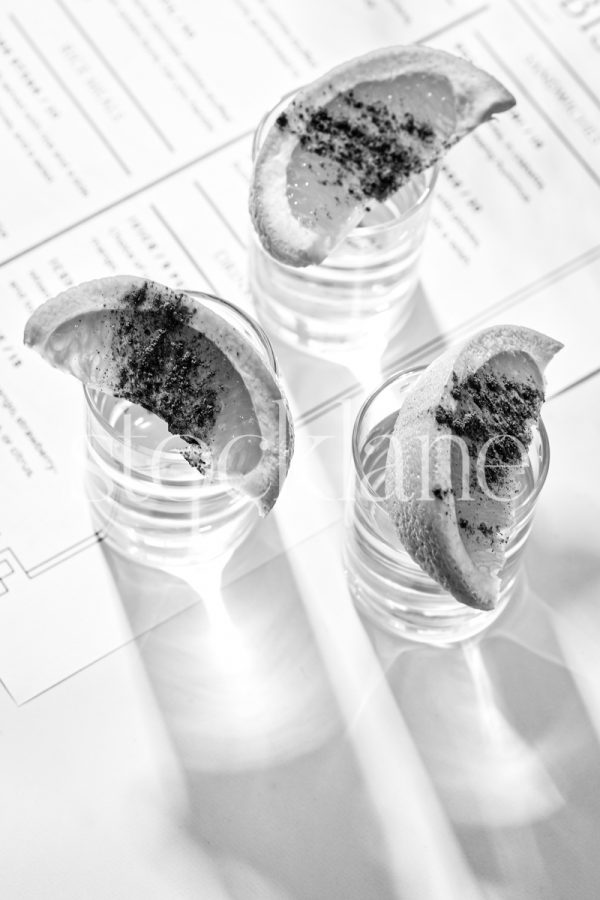 Vertical black and white stock photo of shot glasses with sliced oranges on them on a restaurant menu.