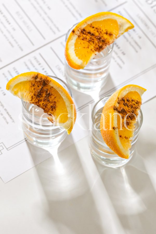 Vertical stock photo of shot glasses with sliced oranges on them on a restaurant menu.