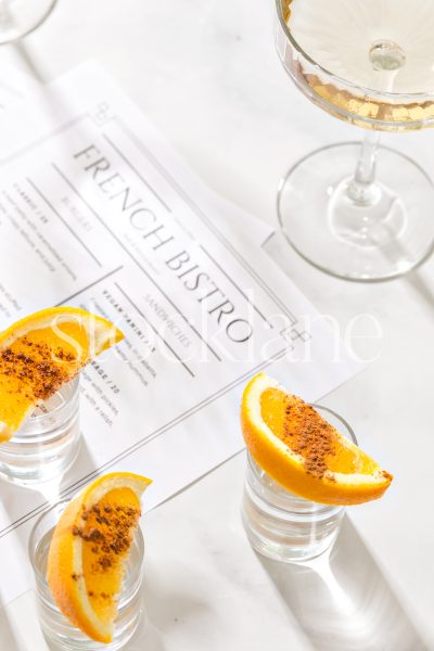 Vertical stock photo of a champagne glass and shots with orange slices on a table top with restaurant menus.