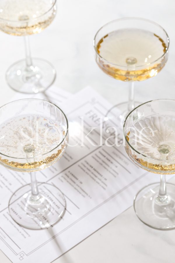 Vertical stock photo of champagne glasses and restaurant menus on a marble tabletop.