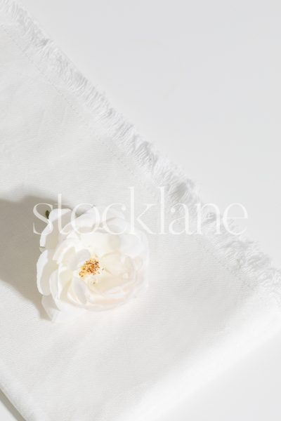 Vertical stock photo of a white rose on a white linen cloth.