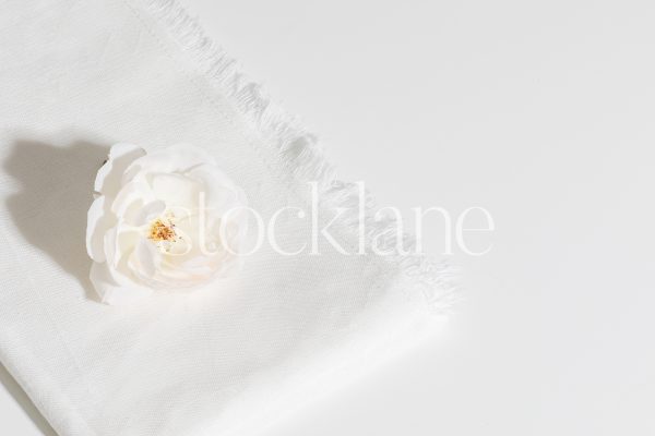 Horizontal stock photo of a white rose on a white linen cloth.