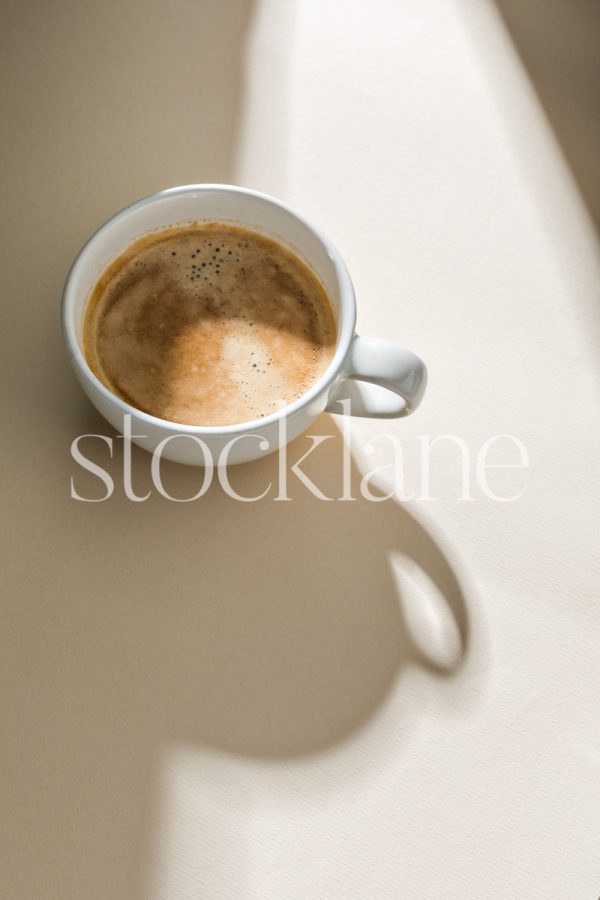 Vertical stock photo of a cup of coffee on a neutral colored background.