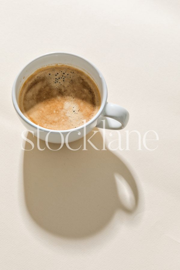 Vertical stock photo of a cup of coffee on a neutral colored background.