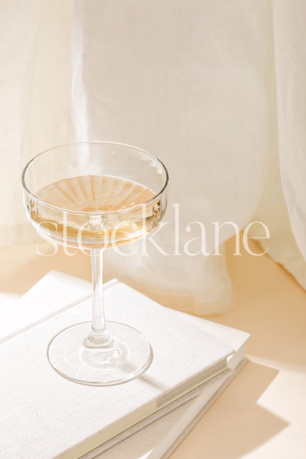 Vertical stock photo of a champagne coupe glass on top of some books.