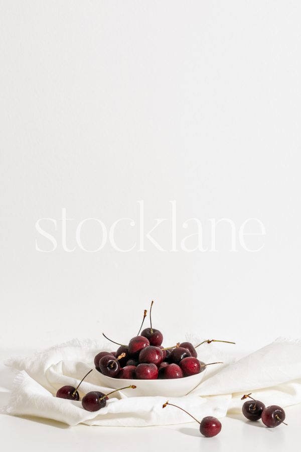 Vertical stock photo of a white bowl with cherries.