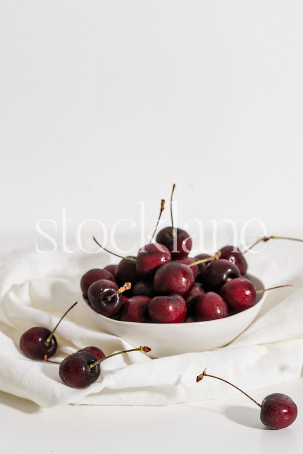 Vertical stock photo of a white bowl with cherries.