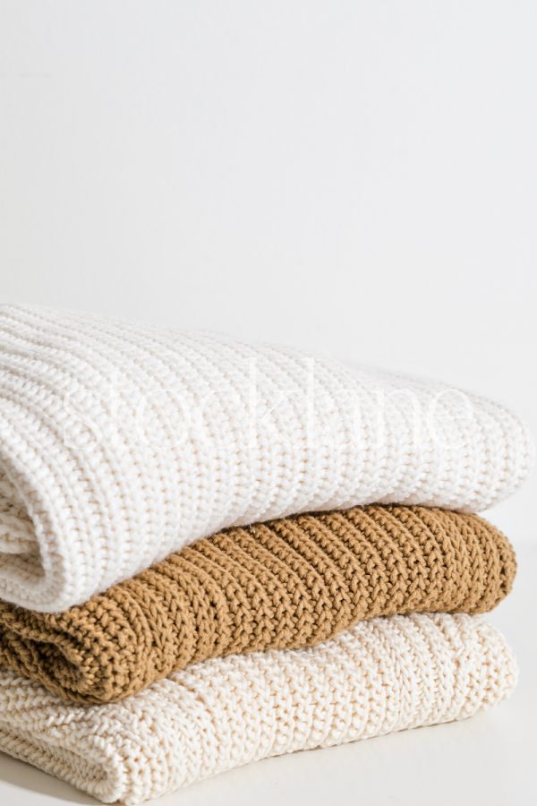 Vertical stock photo of a stack of neutral colored sweaters.