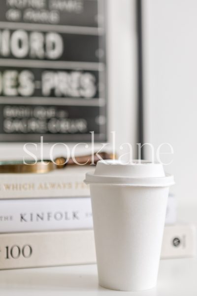 Vertical stock photo of a white disposable coffee cup with books in the background.