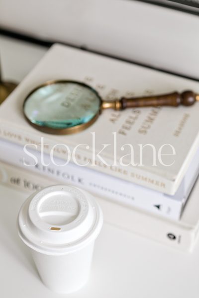 Vertical stock photo of a white disposable coffee cup with books in the background.