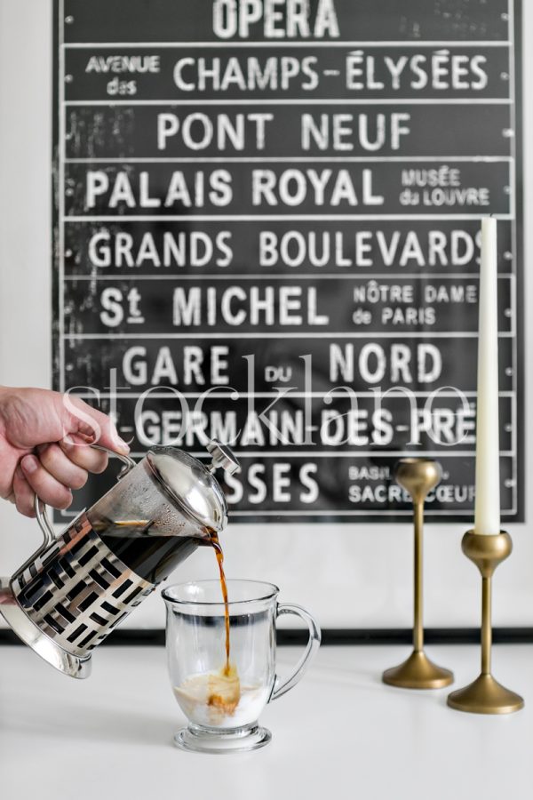 Vertical stock photo of French press coffee being poured into a glass with milk.