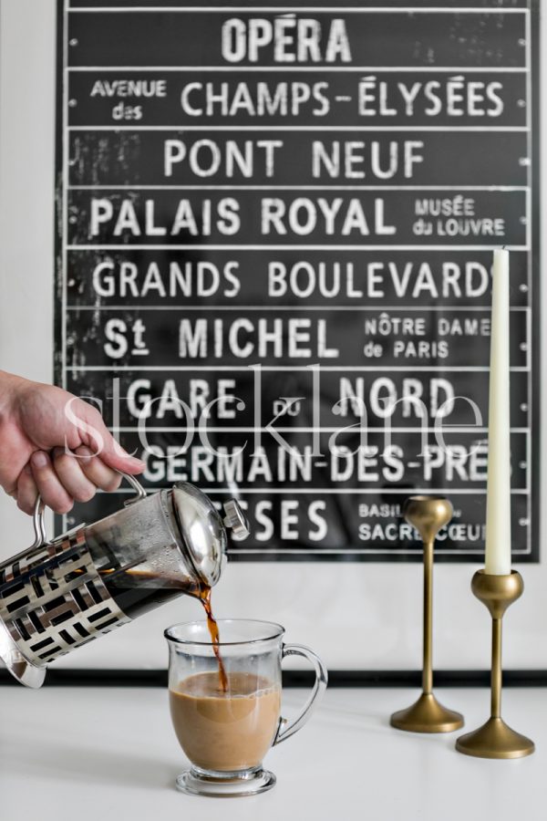 Vertical stock photo of French press coffee being poured into a glass with milk.