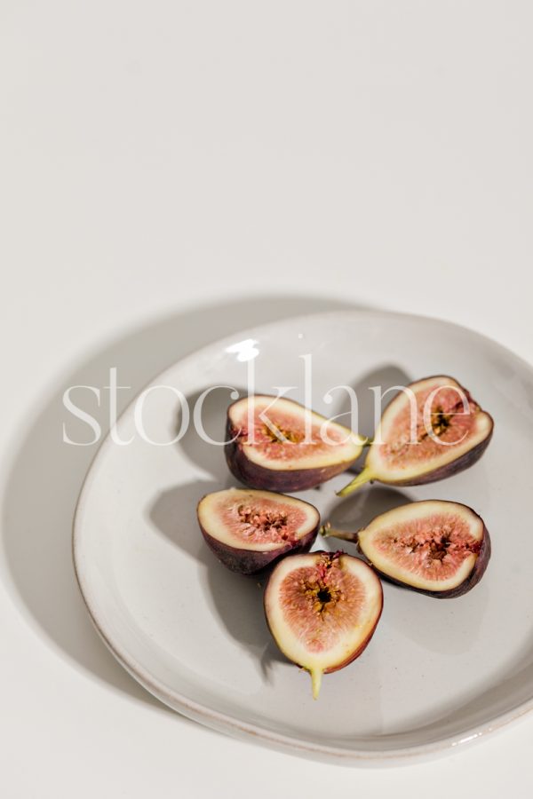 Vertical stock photo of a plate with figs on a neutral colored background.