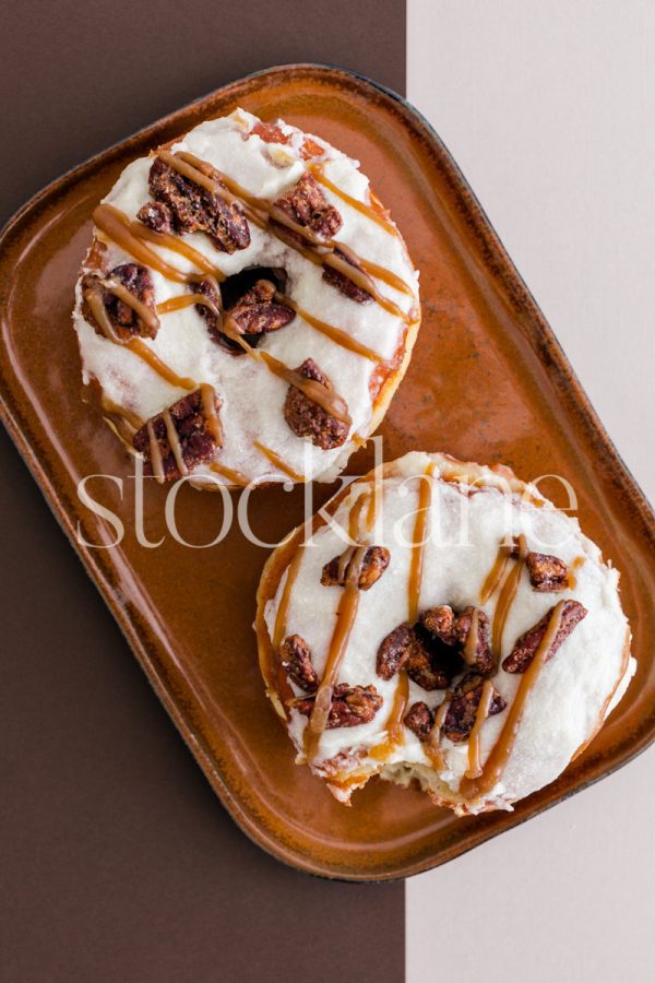 Vertical stock photo of a plate with two fall-themed donuts on a brown and neutral background.