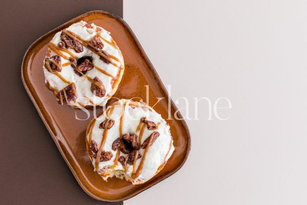 Horizontal stock photo of a plate with two fall-themed donuts on a brown and neutral background.