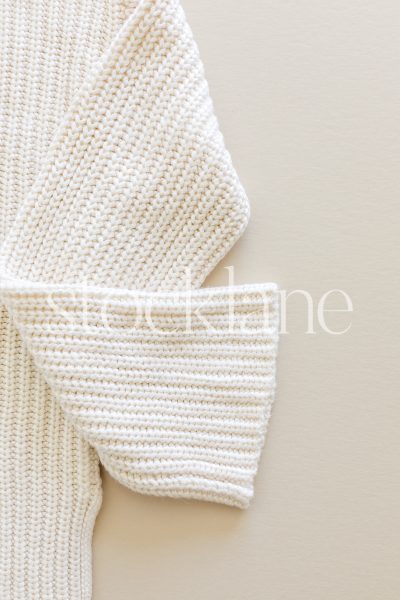 Vertical stock photo of a white sweater on a neutral background.