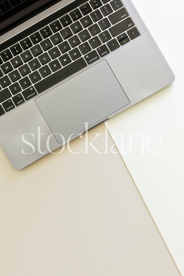 Vertical stock photo of a laptop on a neutral background.