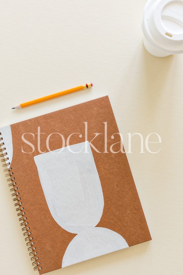 Vertical stock photo of a notebook and coffee on a neutral background.