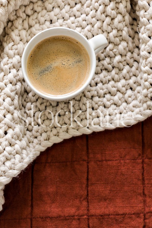 Vertical stock photo of a cup of coffee on a bed.