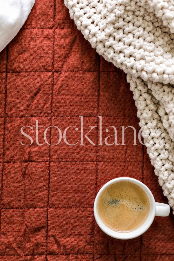 Vertical stock photo of a cup of coffee on a bed.