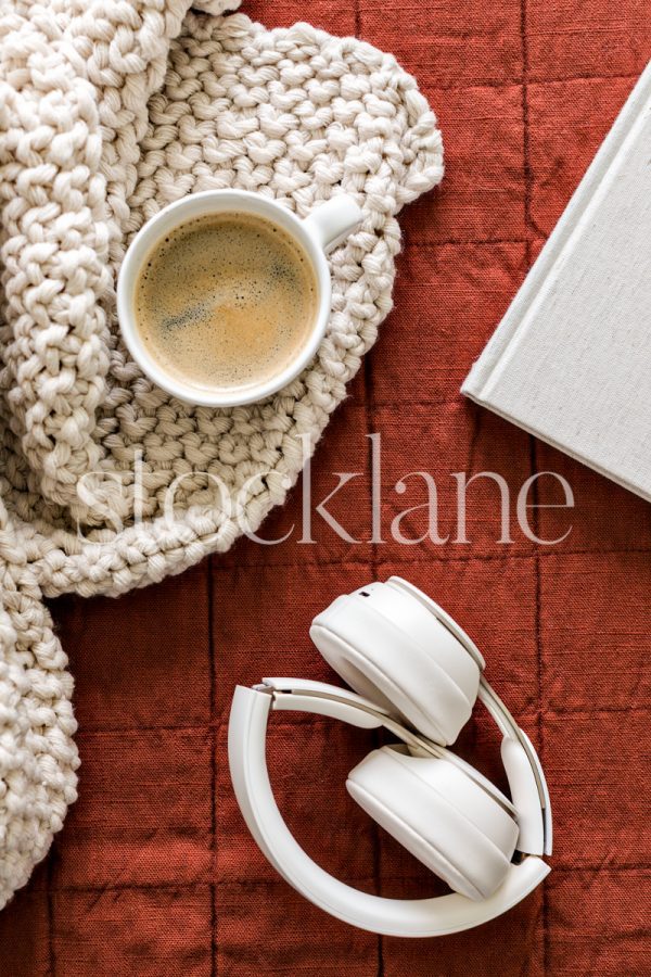 Vertical stock photo of a bed with a blanket, book, coffee and headphones.