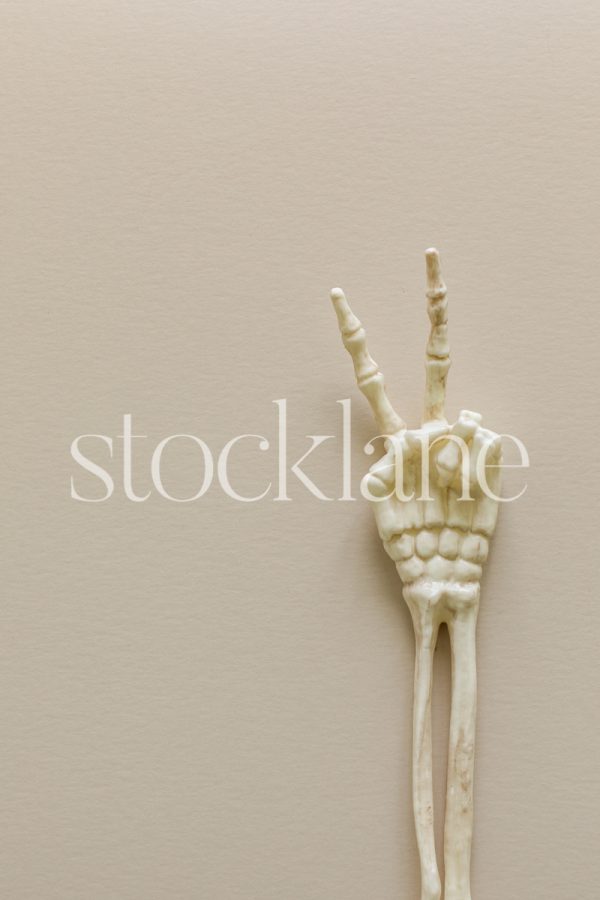 Vertical stock photo of a skeleton arm with peace sign on a neutral background.