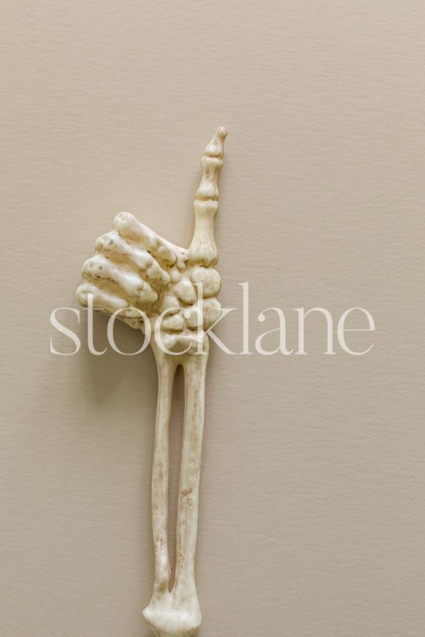 Vertical stock photo of a skeleton arm with thumbs up sign on a neutral background.