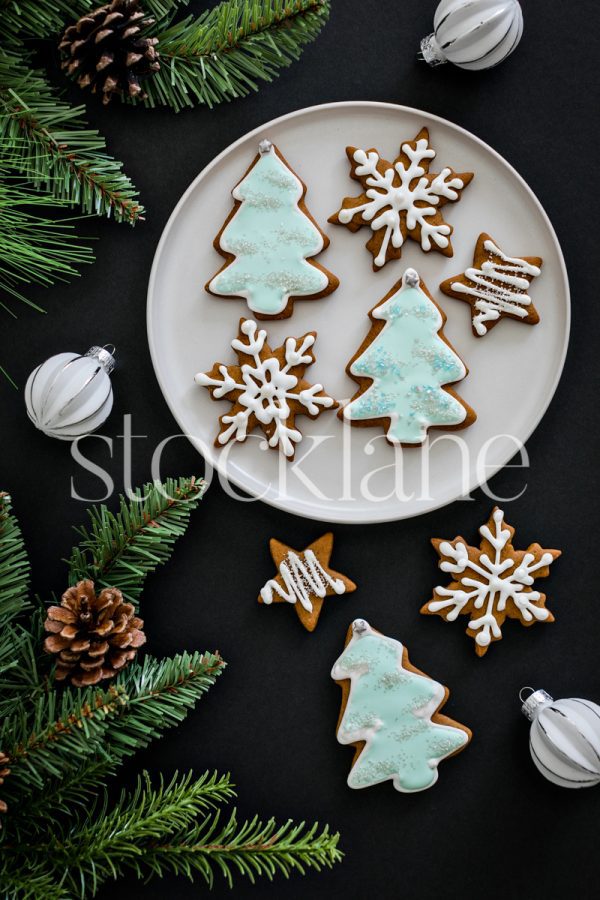 Vertical stock photo of Christmas gingerbread cookies and ornaments on a black background.